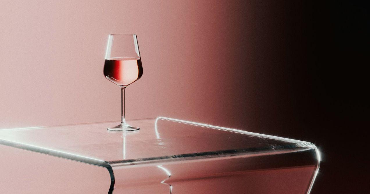 A rose glass of wine on plastic table in a pink background