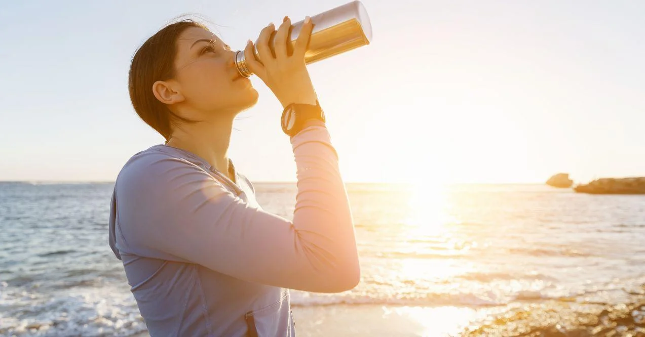 woman drinking water from a metal flask near the sea