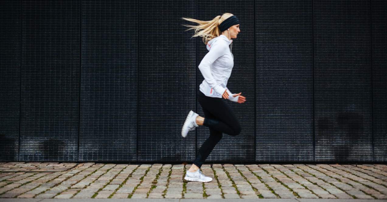 Side view of a sporty young woman running on sidewalk
