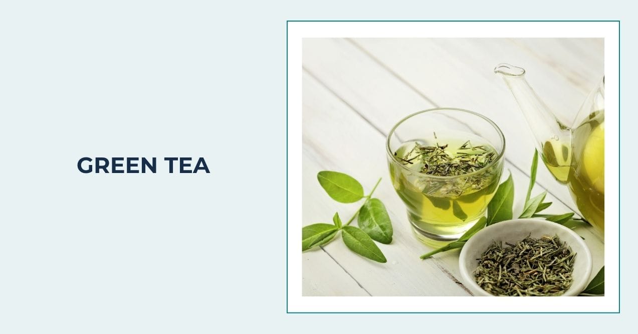Glass cup of green tea with loose leaves and fresh green tea leaves on white table.