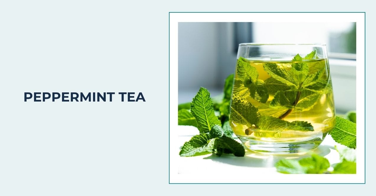 Glass cup of peppermint tea with fresh peppermint leaves inside and around the cup.