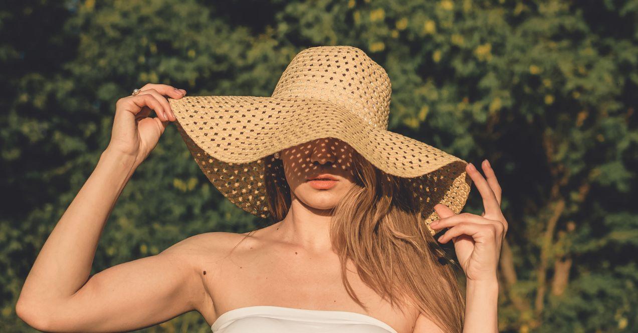 a woman is protecting herself from sun with a hat