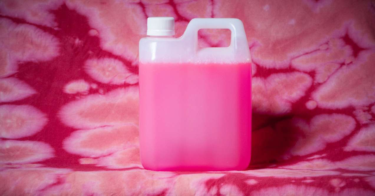 A plastic container filled with pink liquid on a background with a pink tie-dye pattern, suggestive of bleach