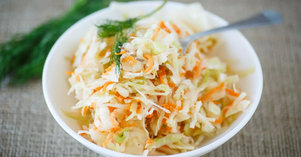 bowl of sauerkraut with shredded carrots and a sprig of dill on top