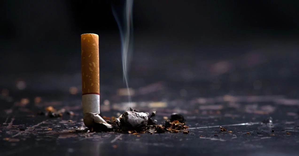 A single lit cigarette with a smoldering tip and rising smoke