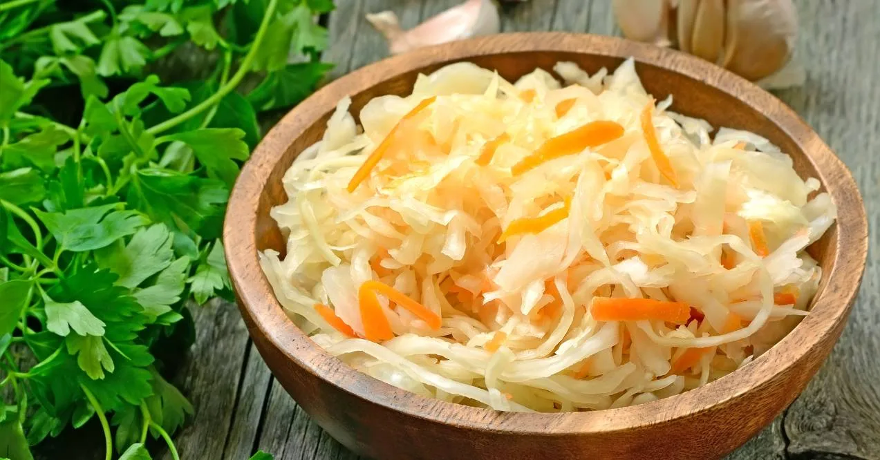 fresh homemade sauerkraut in a wooden bowl on a rustic table garnished with carrot strips next to green parsley leaves