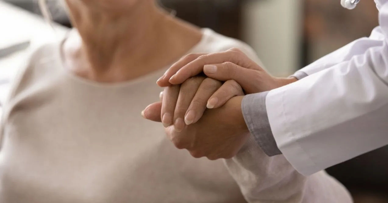 Female doctor in white coat holding hand of senior patient