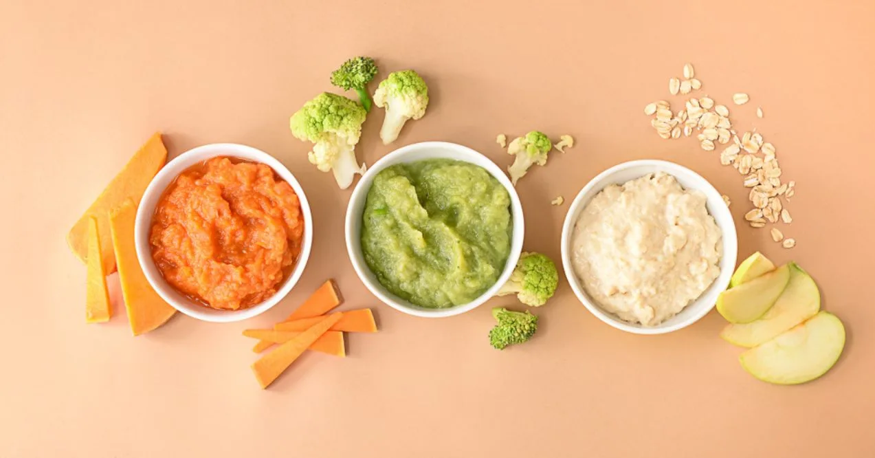 Assorted bowls of mashed food including carrot puree, broccoli puree, and oatmeal
