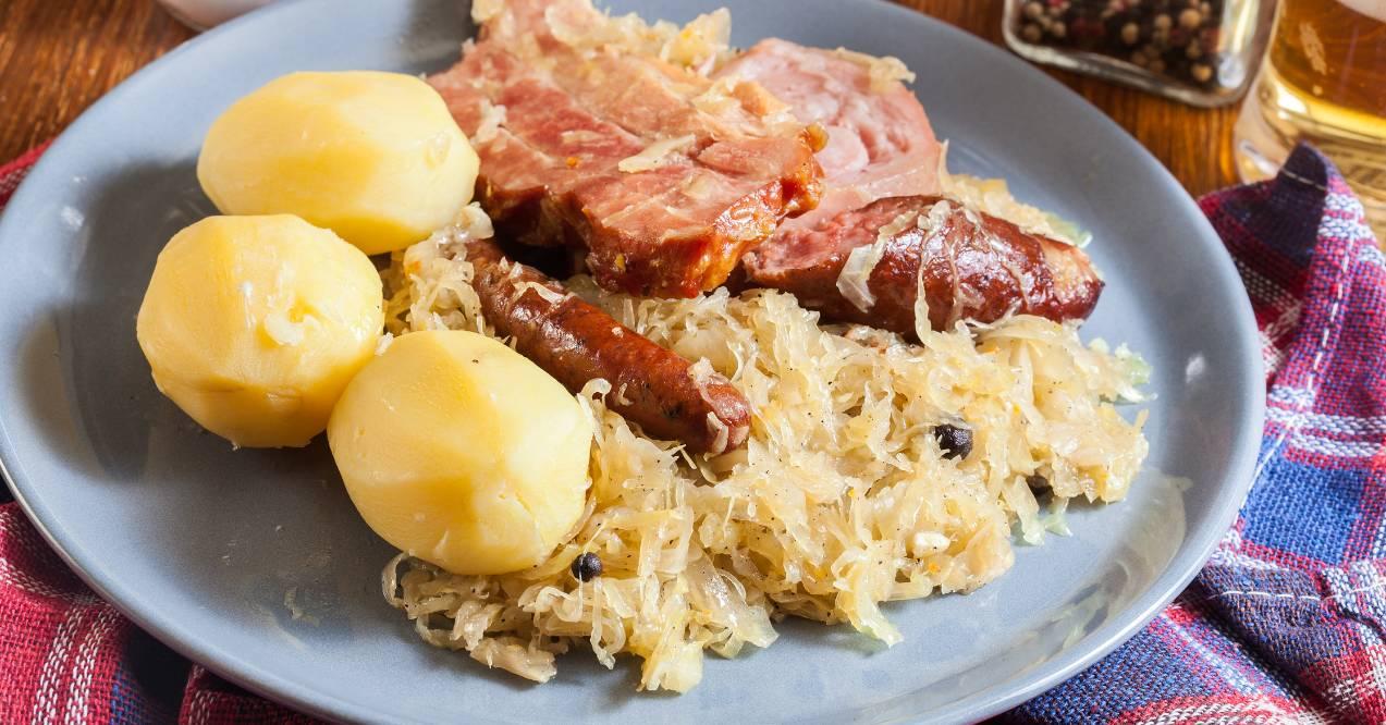 plate of traditional sauerkraut with slices of smoked ham and sausage accompanied by boiled potatoes