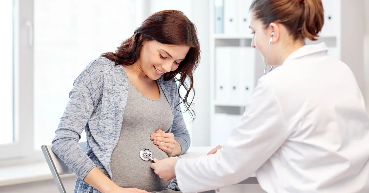 pregnant woman smiling while a doctor listens to her belly with a stethoscope