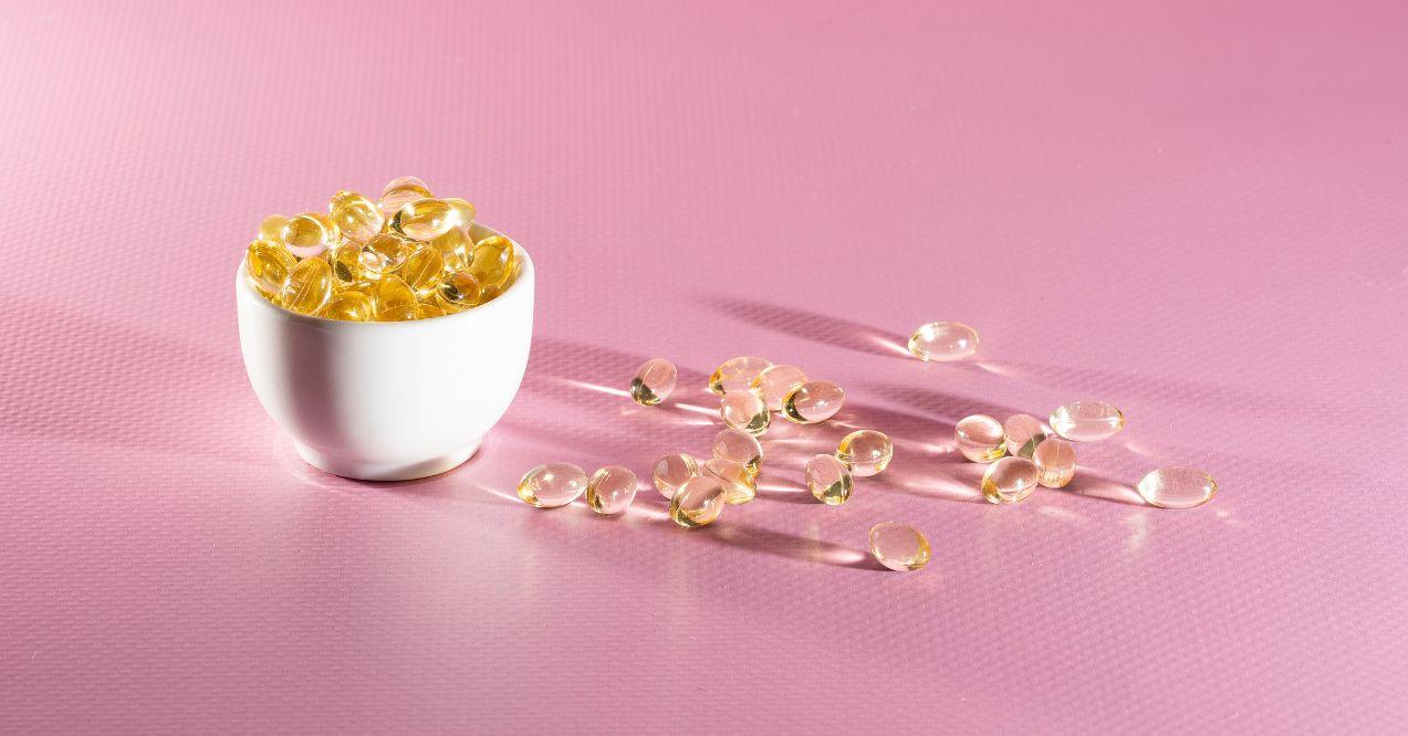 A bowl of vitamin A capsules on a pink background
