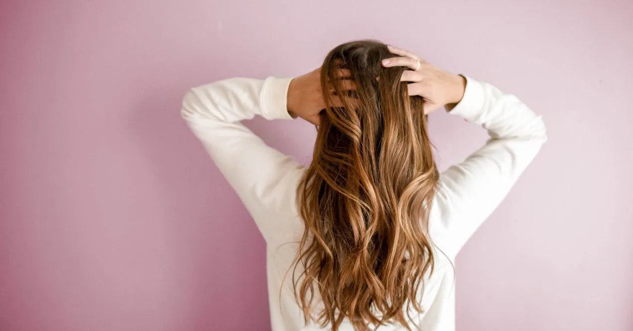 woman with long hair holds her head from behind against a pink background