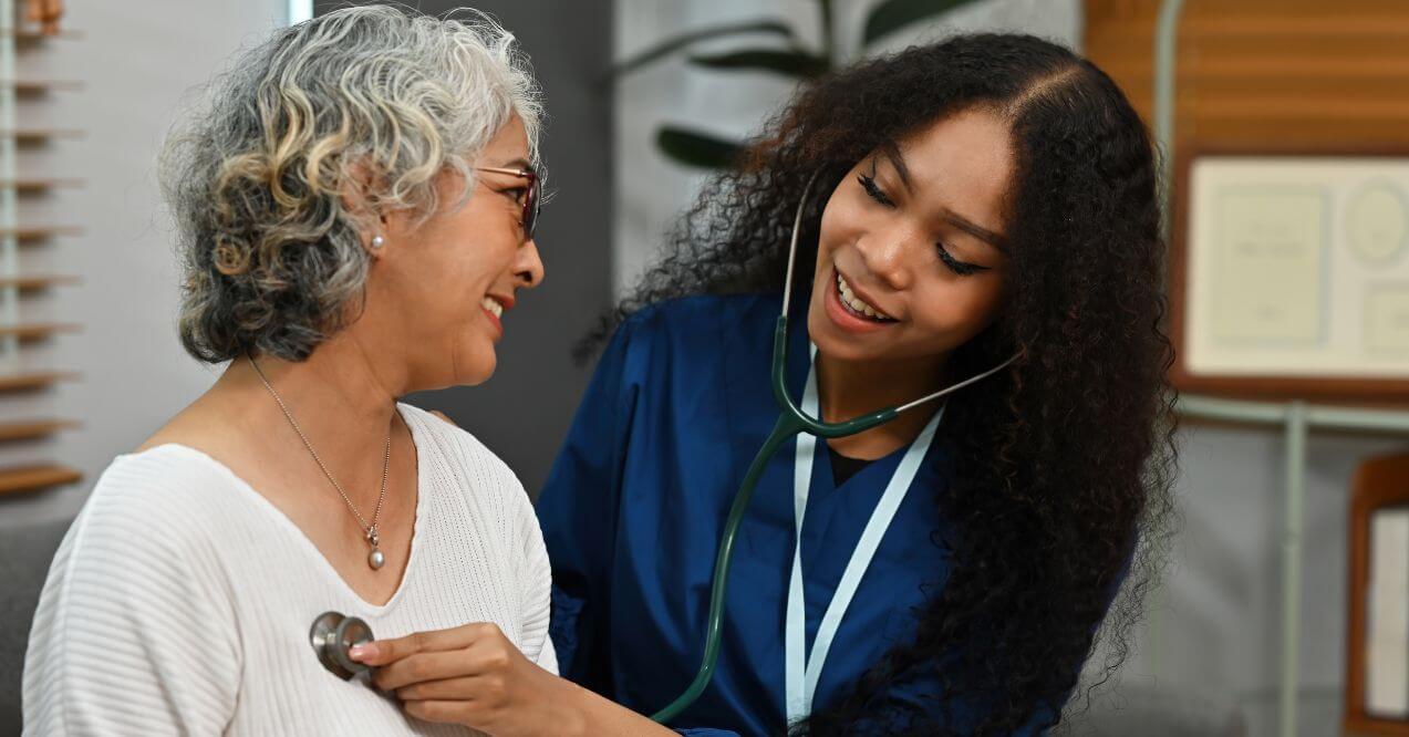 Elderly woman smiling during check-up with female doctor using a stethoscope resembling the regular health check-ups importance for women's health