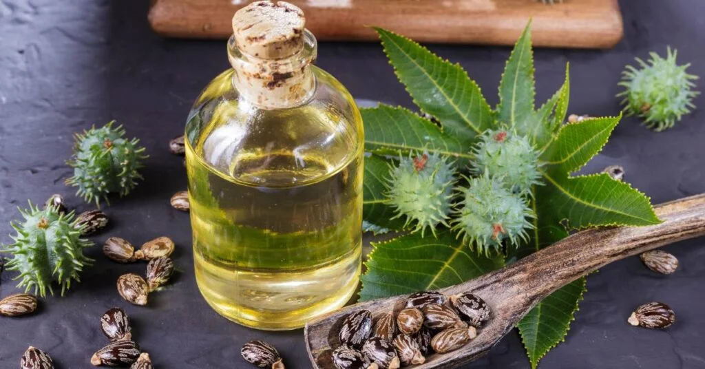 bottle of golden castor oil with cork surrounded by castor beans