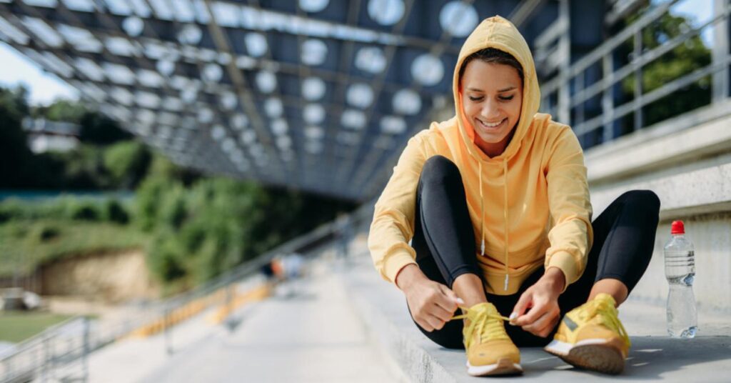 Woman in yellow sweater adjusting her laces on sneakers before workout