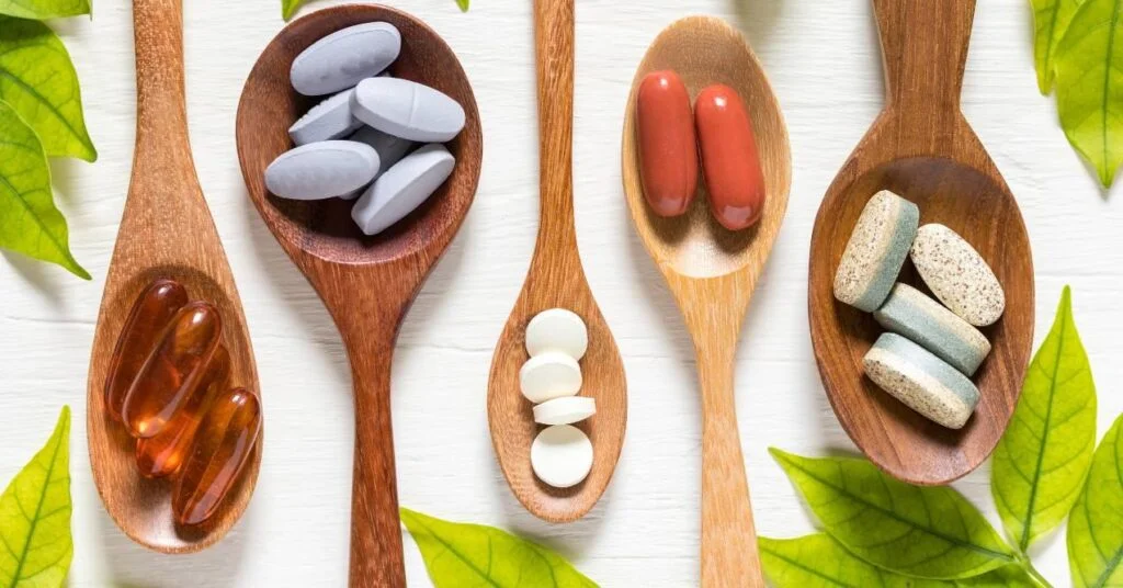 different types of supplements are displayed on wooden spoons, flanked by green leaves on a white background