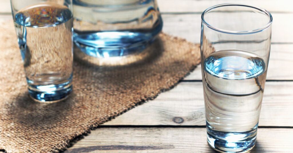 Three glasses of water placed on a rustic wooden table with a burlap cloth beneath them