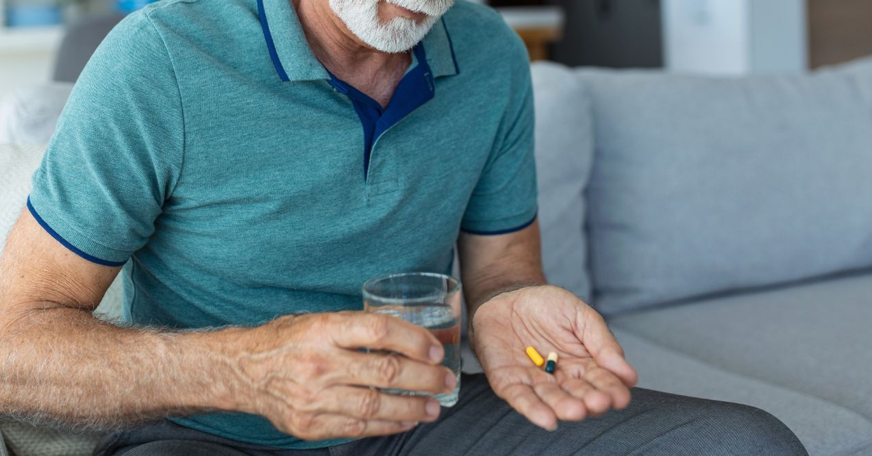 Senior man takes pill with glass of water in hand