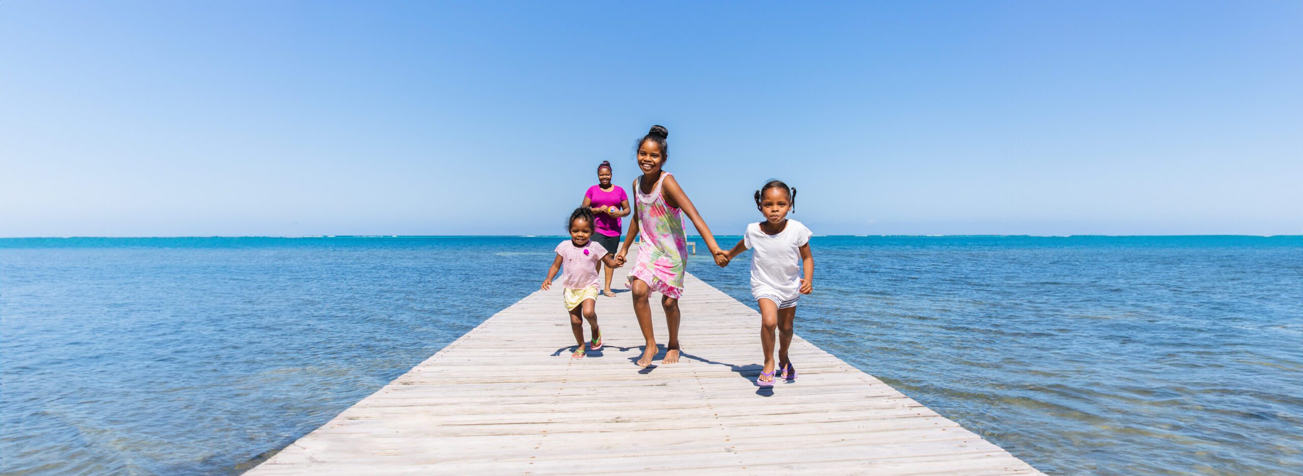 three children running joyfully on a wooden pier beside a blue sea under a clear sky