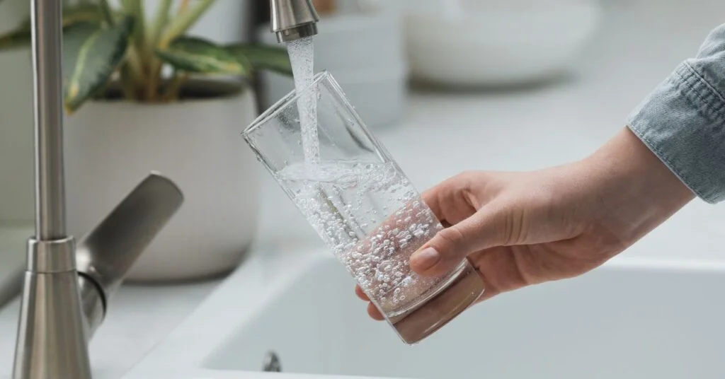 Hand holding a glass while pouring water from the tap