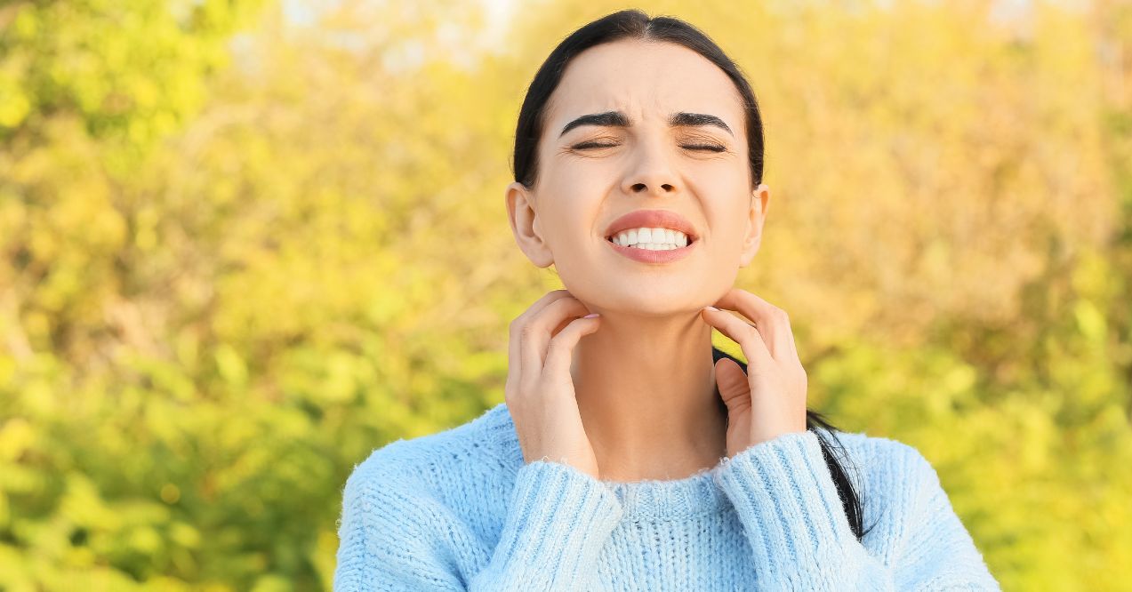 a woman scratching her neck outdoors, indicating potential skin irritation or dryness that olive oil can help alleviate as a natural remedy.