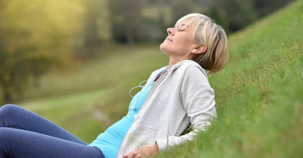 Middle aged beautiful blonde woman sitting on the glass breathing, enjoying life