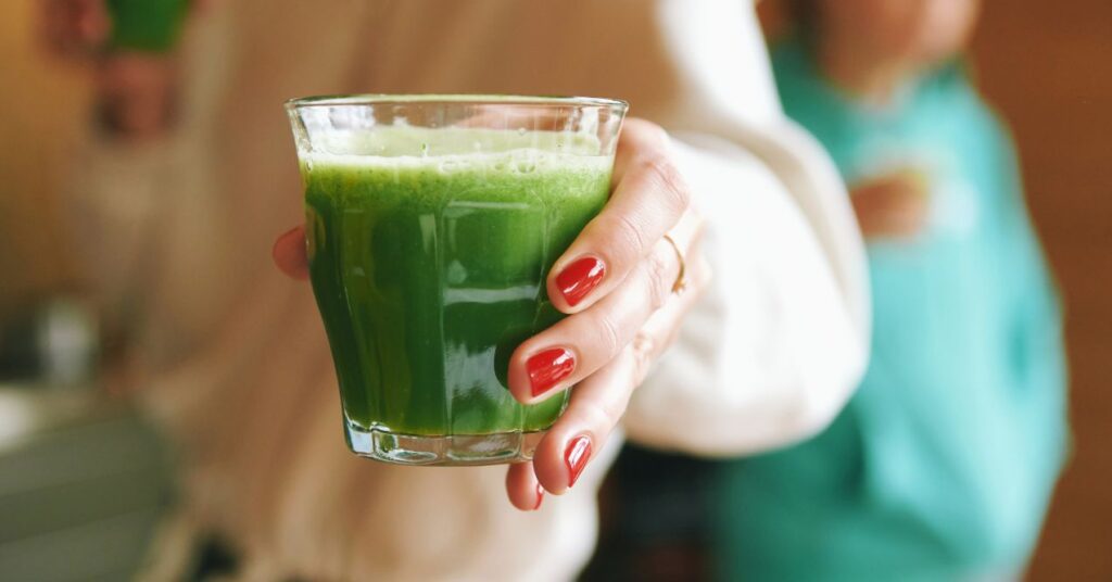 Women hand holding a glass of green juices that are good for lymph health