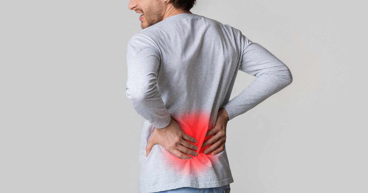 a man in a gray long-sleeve shirt experiencing back pain, indicated by a red highlighted area on his lower back.