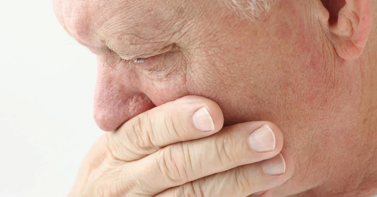 nauseated mature man holds hand up to mouth