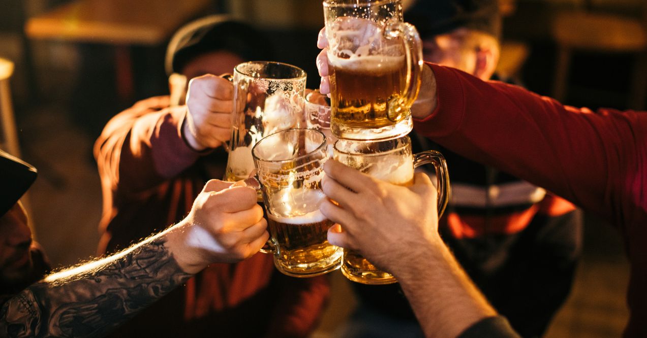 group of friends raising beer mugs in a toast, with various tattoos visible on their arms.