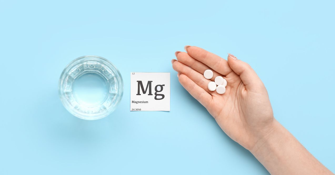 A hand with white pills and magnesium sign next to a glass of water in a blue background