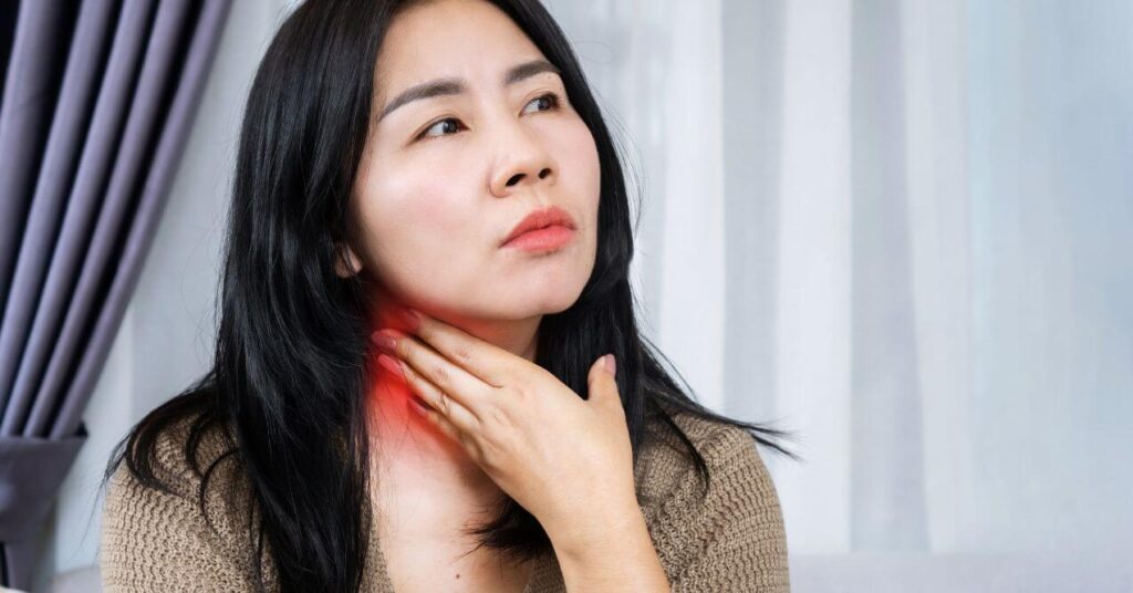 Woman checking her neck for swollen lymph nodes with redness and discomfort visible on her throat.