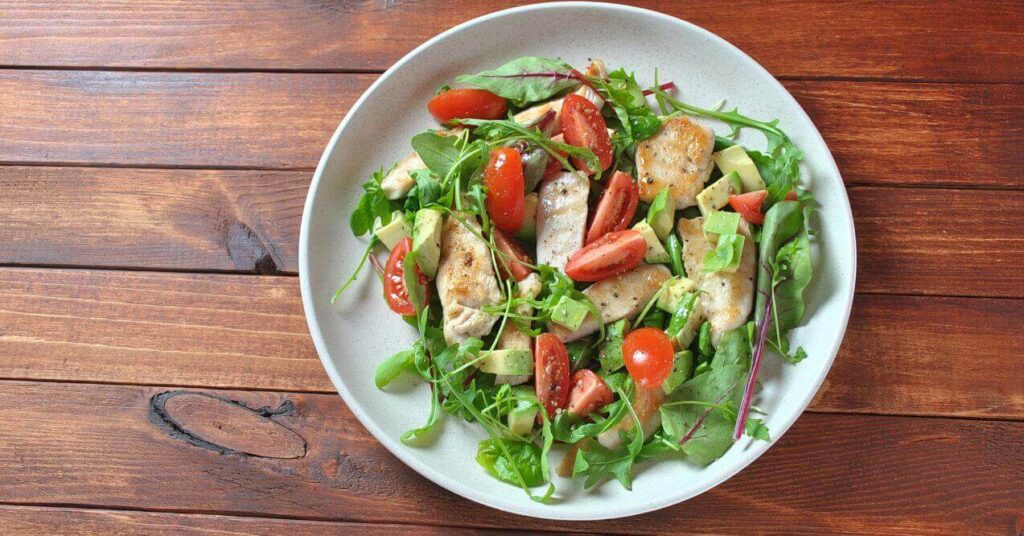 Fresh chicken salad with avocado, cherry tomatoes, and mixed greens on a white plate.