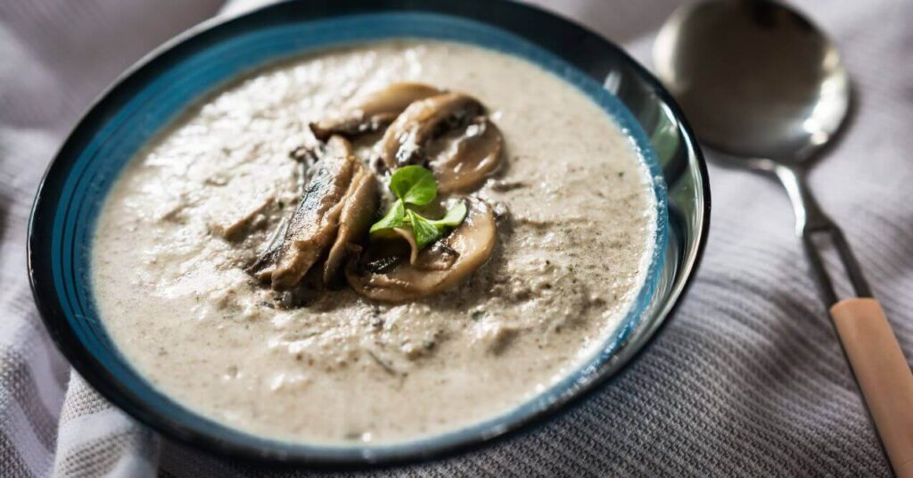 Creamy dairy-free keto chicken and mushroom soup served in a blue-rimmed bowl with sliced mushrooms on top.