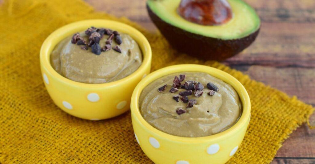 Creamy dairy-free keto chocolate avocado mousse topped with cacao nibs in yellow polka dot bowls.