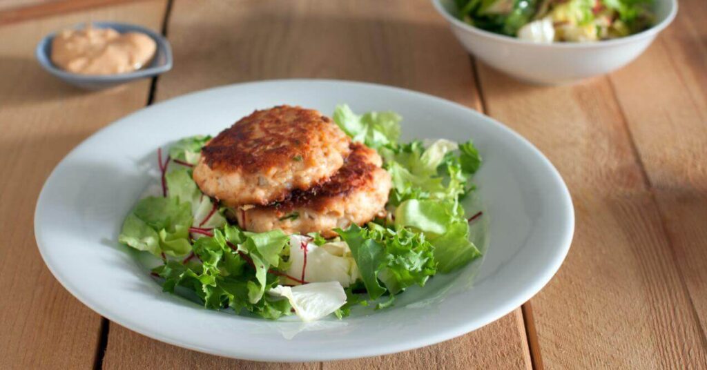 Crispy dairy-free keto salmon patties served on a bed of fresh greens.