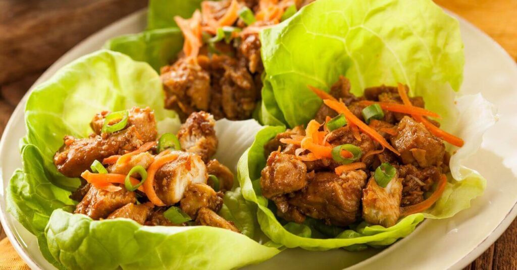 Keto peanut chicken wraps served in crisp lettuce cups, topped with shredded carrots and green onions.