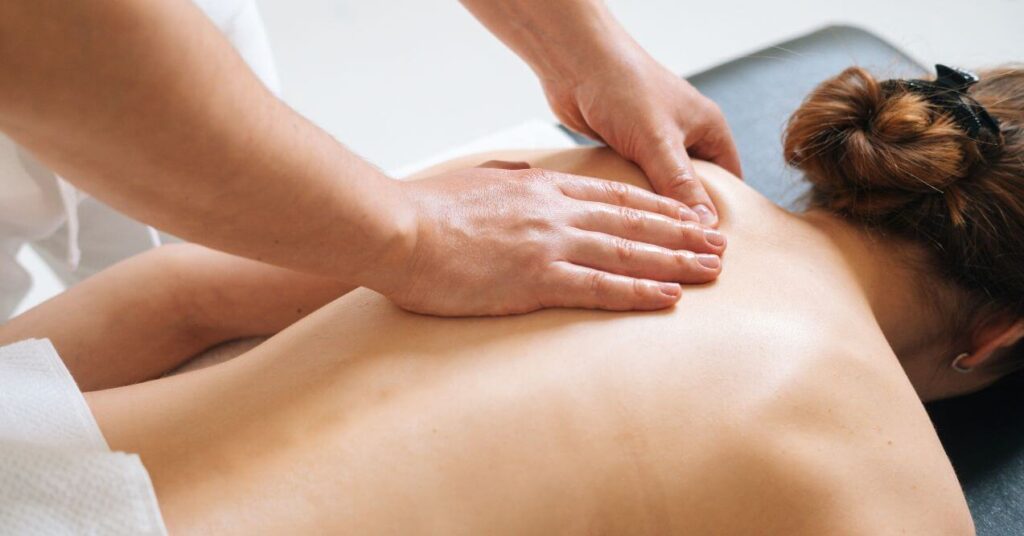 A person receiving a relaxing back massage from a therapist. The therapist's hands are gently working on the muscles of the client's upper back in a peaceful setting.