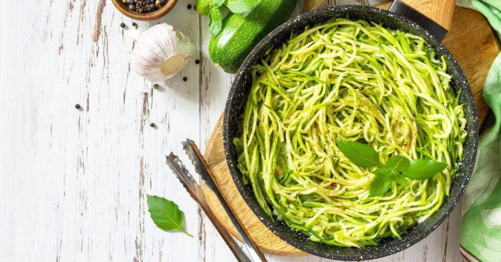 Zucchini noodles with dairy-free pesto in a black skillet, garnished with fresh basil.