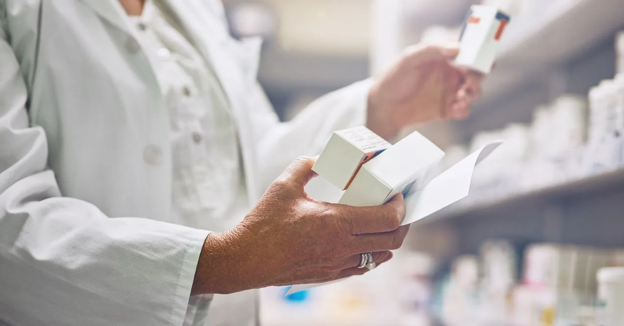 Pharmacist is holding a box for supplements with document at shelf for medicine, check and inventory for health.