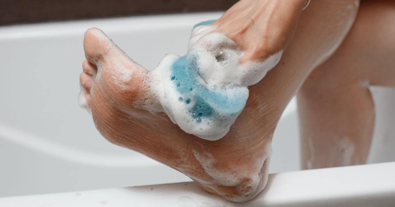 Close-up of a person washing their foot with soapy foam and a scrubber.