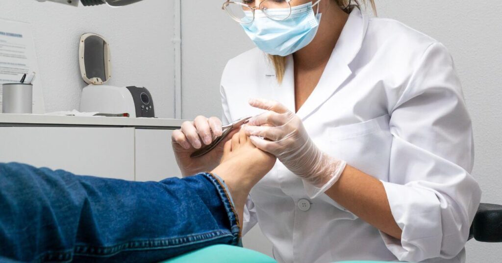 Young podiatrist wearing a mask and gloves is cutting toe nails for a patient.