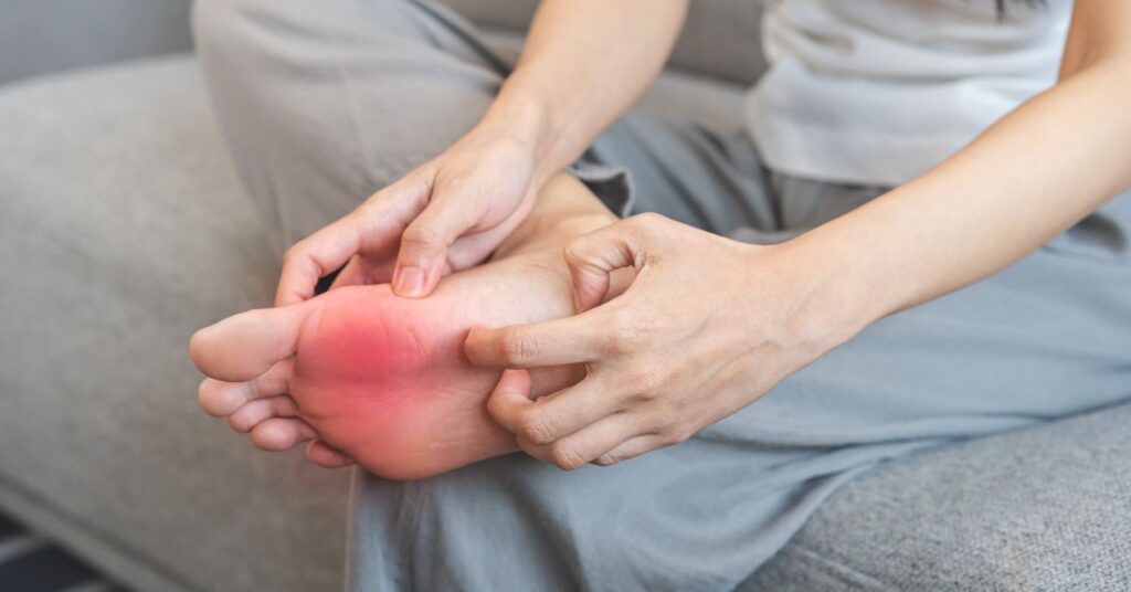 Woman seated on a couch touching her foot, which are red, because of the pain.