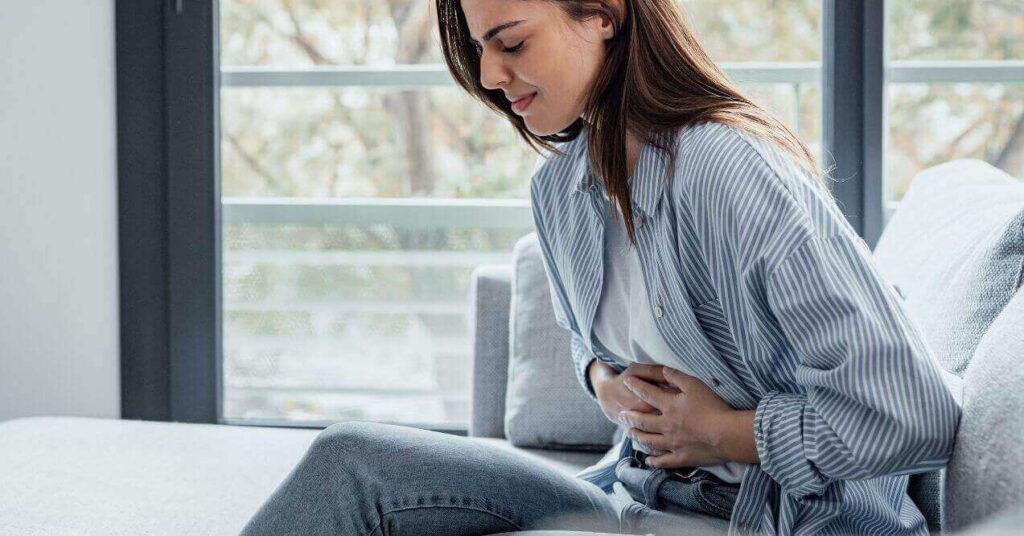 Sick young woman sitting down and being in pain, holding her stomach.