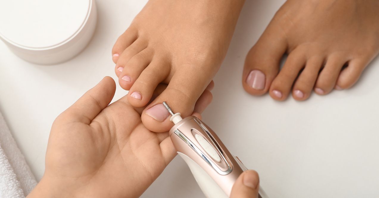 Person receiving a pedicure with an electric nail file on their toenail.