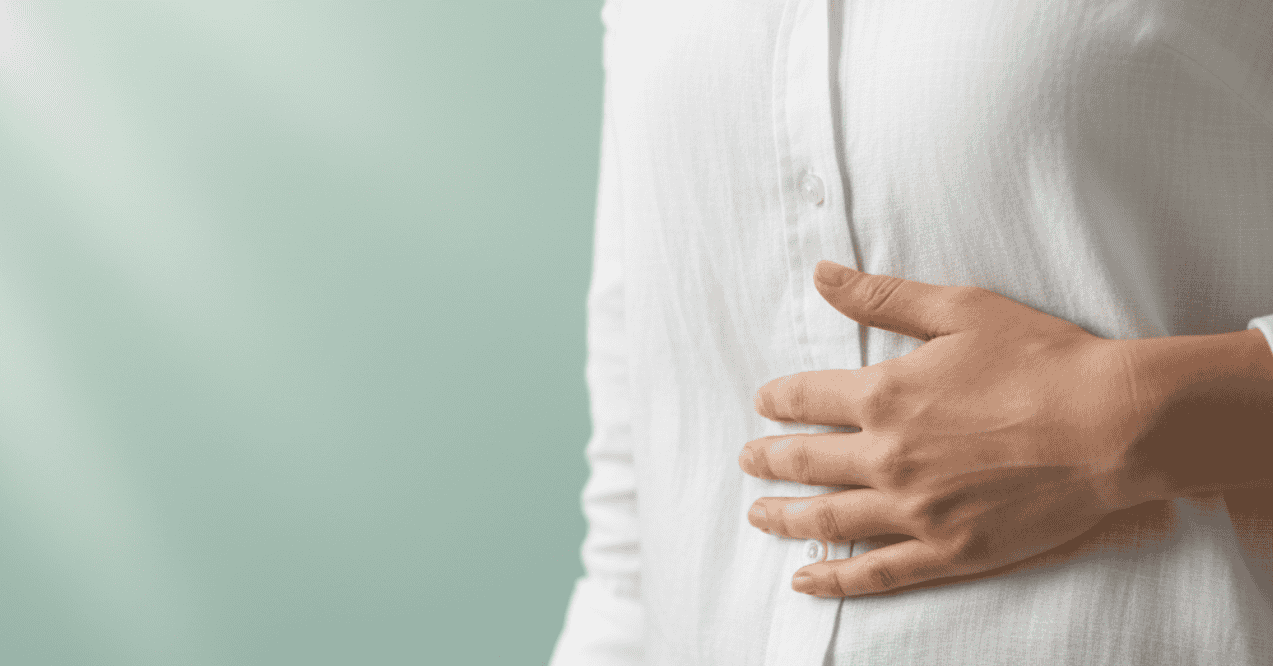 Close-up of a person's hand on their upper right abdomen (gallbladder area) against a mint green background.