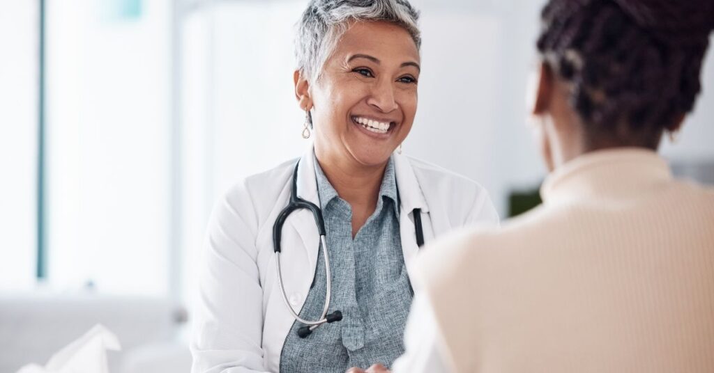 Smiling healthcare professional with a stethoscope around her neck speaking with a patient during a consultation.