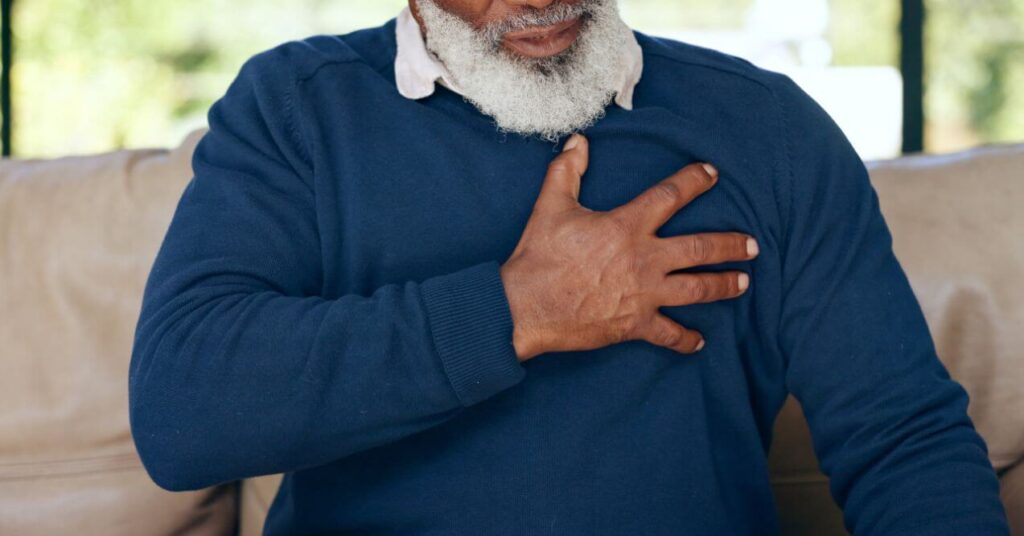 Elderly man holding his chest, experiencing discomfort from heartburn.