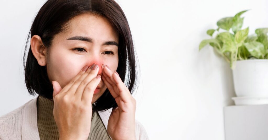 Woman touching her nose, which appears red and irritated, possibly due to itching or allergies.