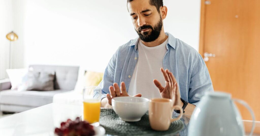 Man sitting at a table, pushing away food, indicating a loss of appetite.